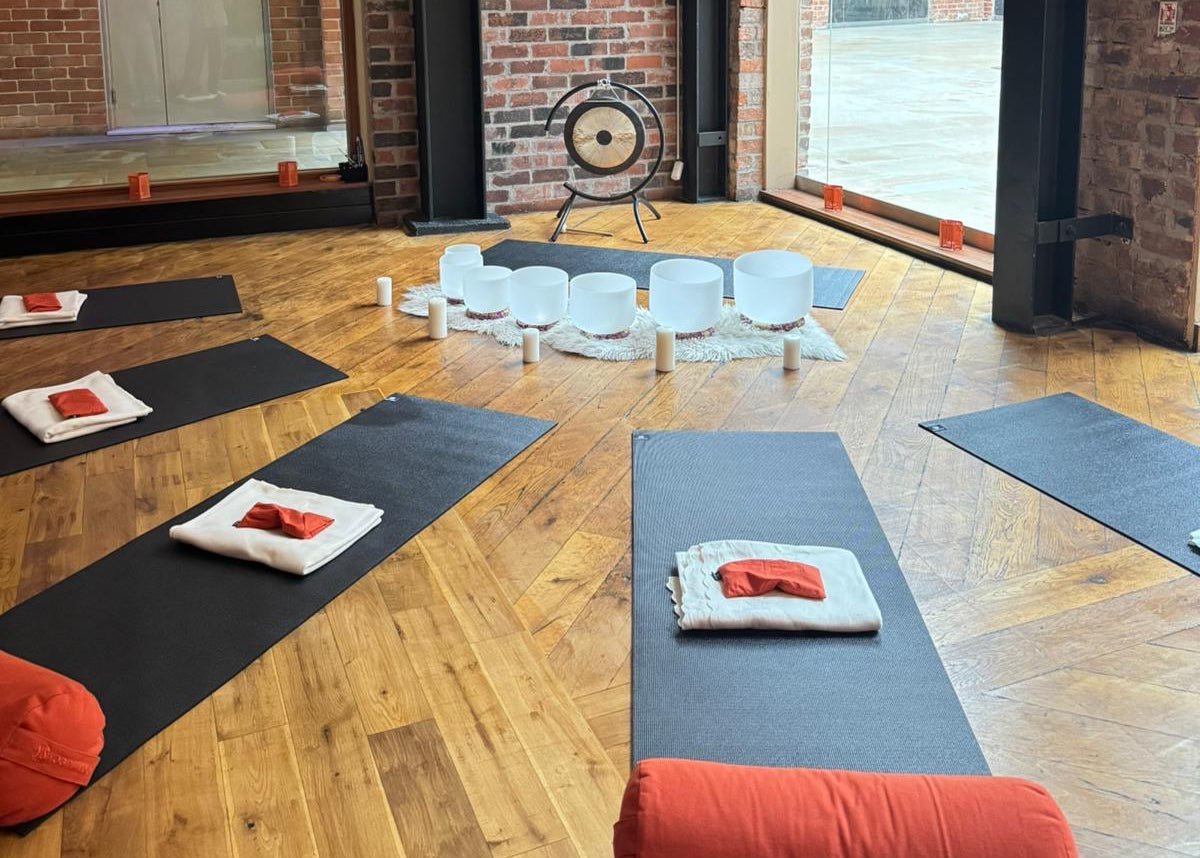 Yoga studio with mats, pillows, and a gong on a wooden floor.